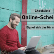 Checkliste - Online-Scheidung - Eignet sich das für mich? : Mann mir rotem Pulli sitzt vor hellblauer Wand an seinem laptop und lächelt glücklich